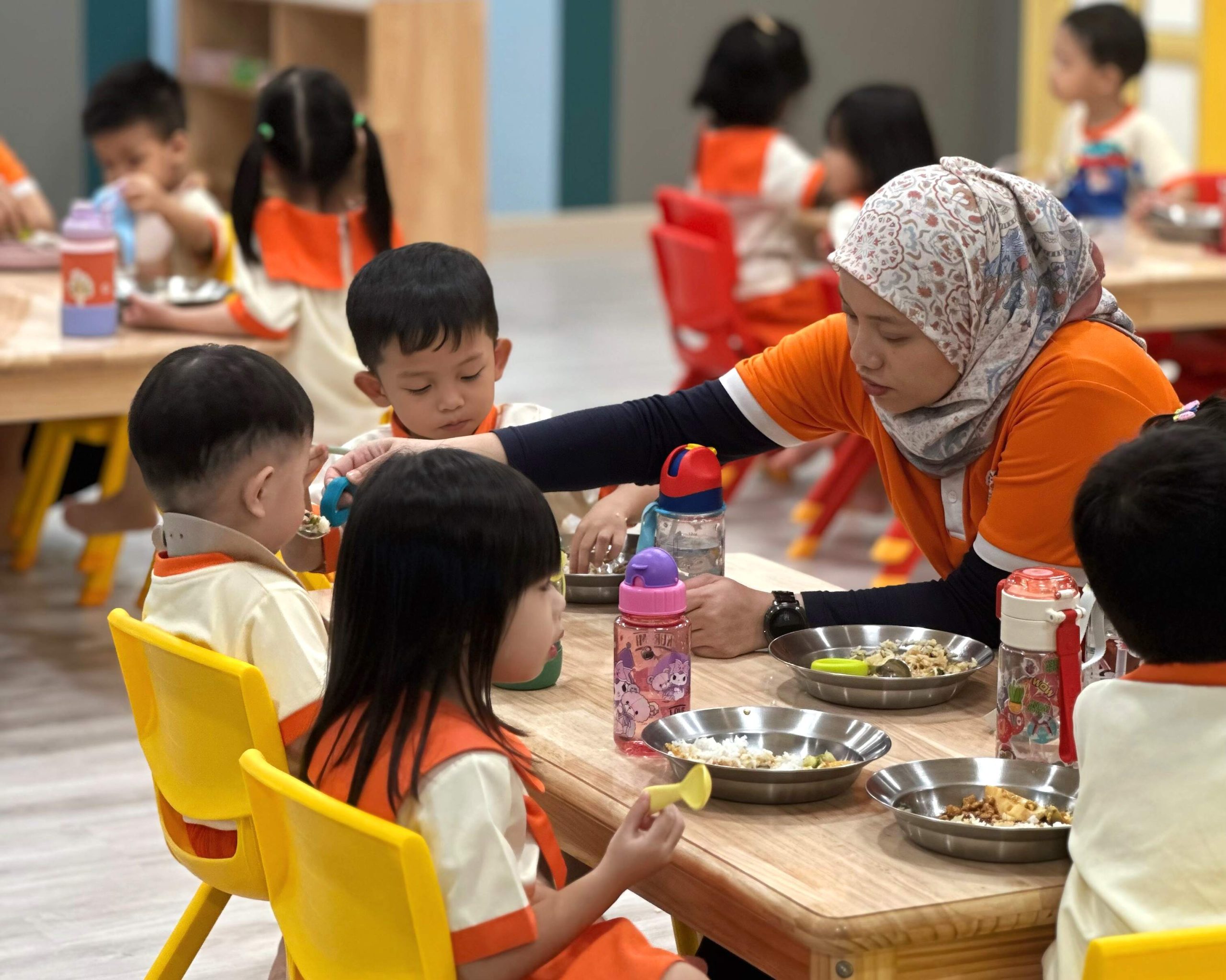 Preschool teachers feeding toddler in a Taska